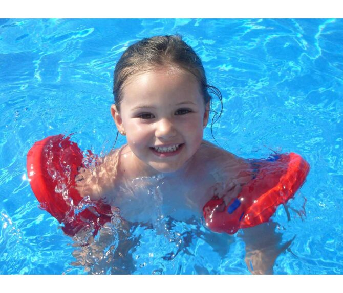 Niña sonriente en la piscina con Manguitos flotador Delphin